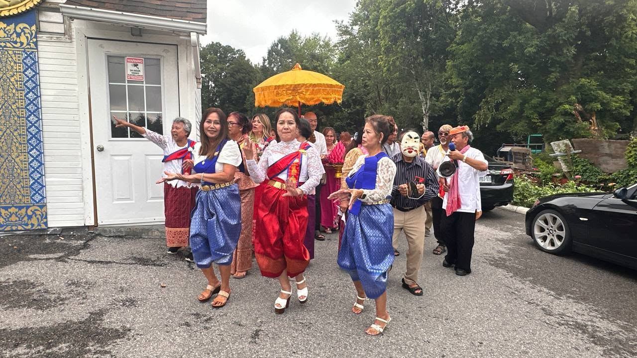 Women in traditional Khmer silk dancing in a procession under a golden umbrella outside the temple