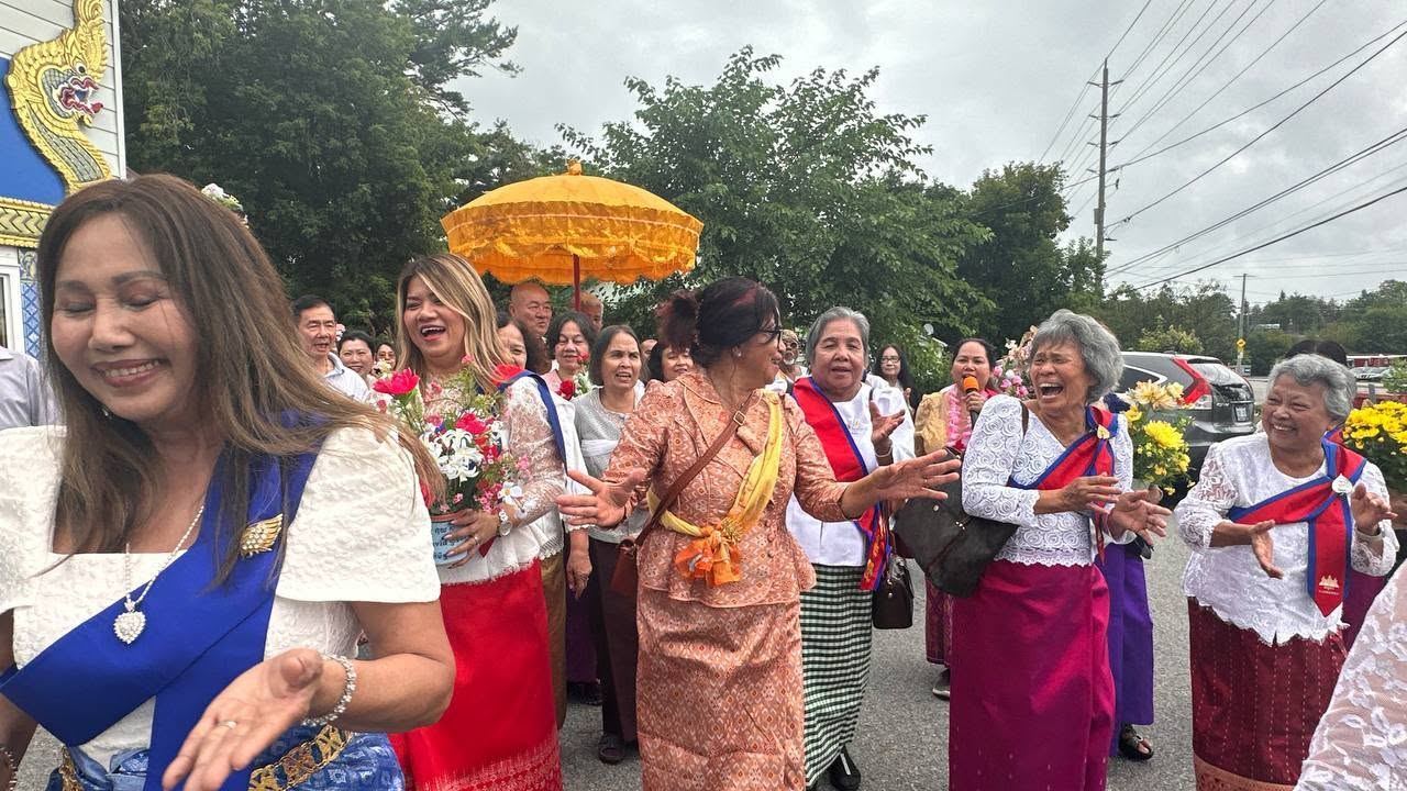 A woman in a blue sash laughing as the procession passes, golden umbrella behind her