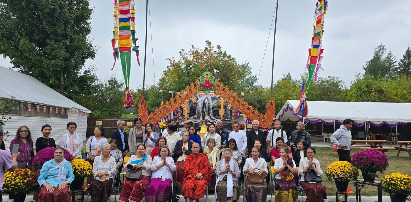 A monk and elders seated before a decorated gateway with colourful banners and chrysanthemums