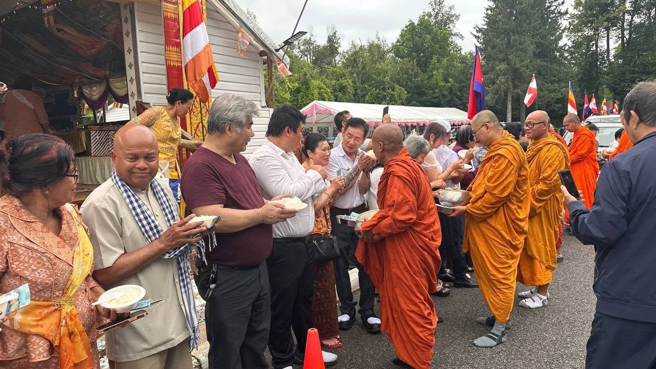 Monks in saffron robes receiving food offerings from a line of community members