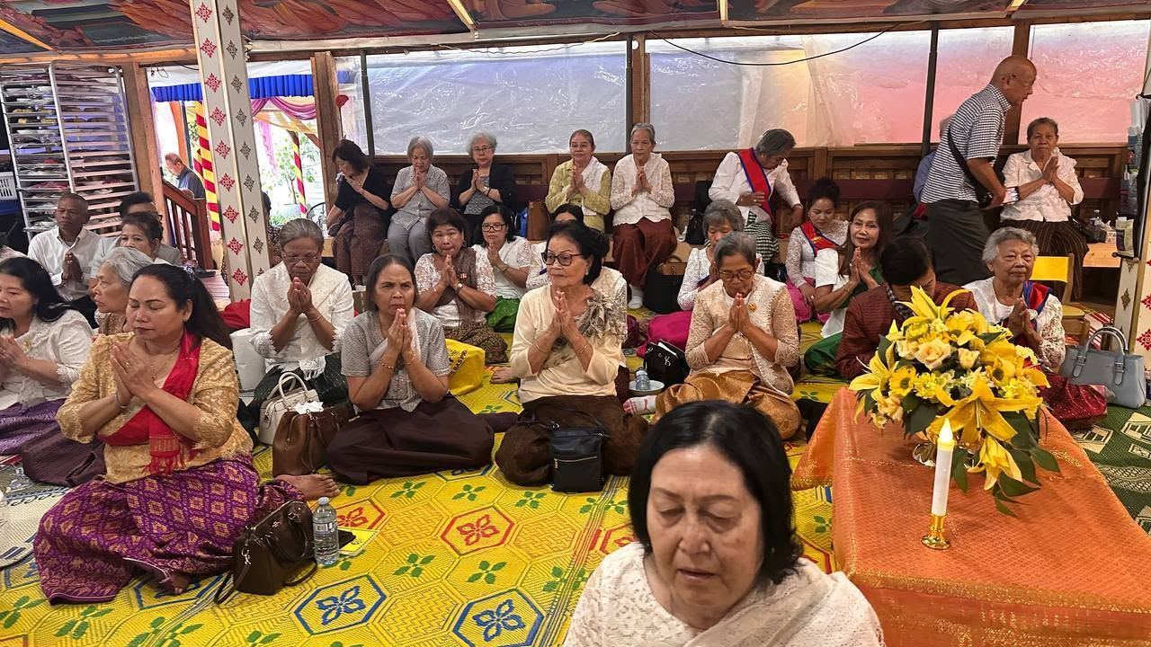 Elders and families praying with their hands together on yellow mats in the festival tent