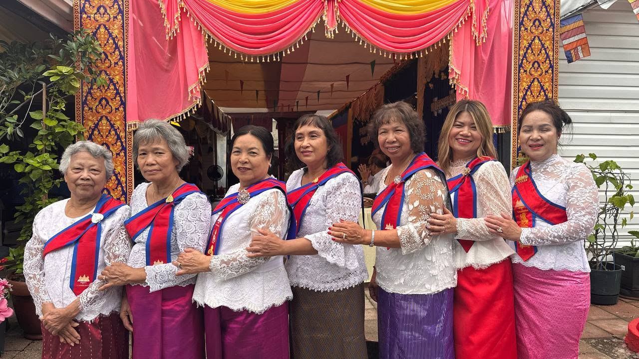 Seven women in white lace blouses and red and blue sashes standing arm in arm