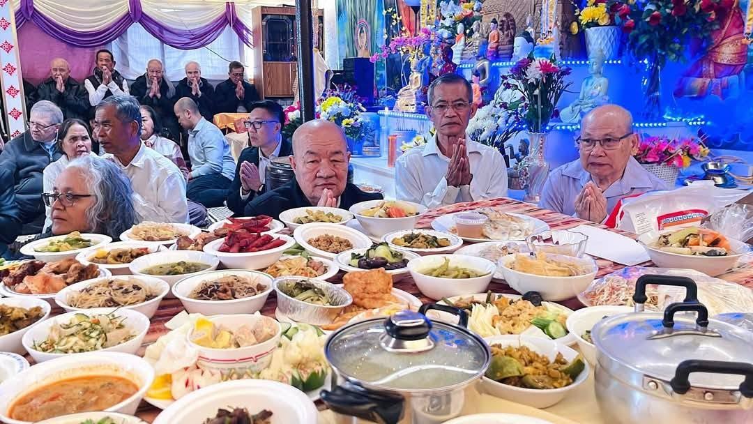 Elders praying behind a table of home-cooked dishes, in front of the lit shrine
